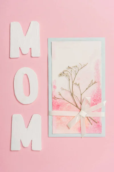 Happy mothers day postcard decorated with dried plant and lace ribbon, and paper word mom on pink background — Stock Photo