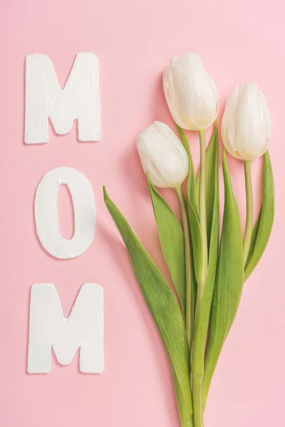 White tulips and paper word mom on pink background — Stock Photo
