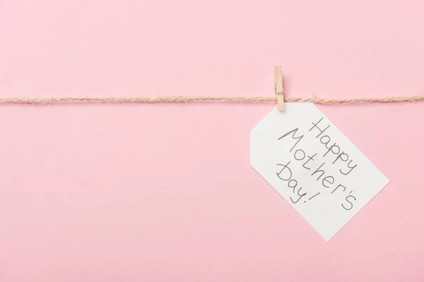 Etiqueta de papel blanco con felicitación feliz día de las madres con hilo grueso sobre fondo rosa - foto de stock