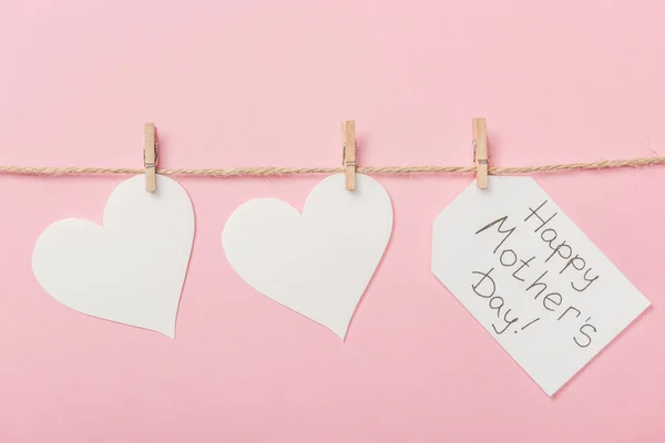 White paper hearts and label with happy mothers day greeting with coarse thread on pink background — Stock Photo
