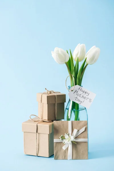 Caixas de presente, cartão de saudação e buquê de tulipas brancas com etiqueta feliz dia das mães no fundo azul — Fotografia de Stock