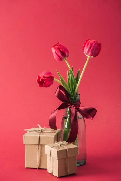 Strauß roter Tulpen mit roter Satinschleife und Geschenkschachteln auf rotem Hintergrund — Stockfoto