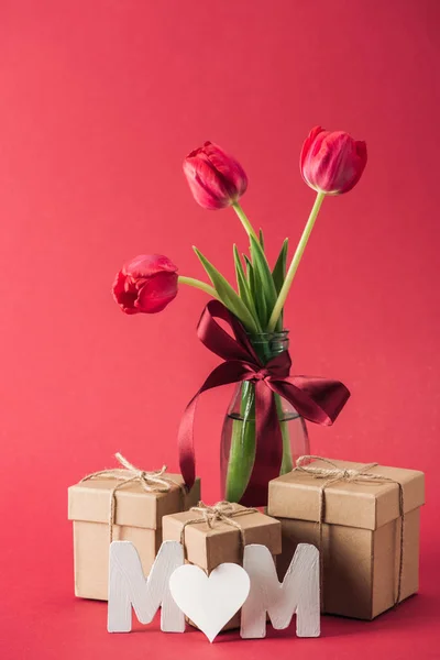 Gift boxes, bouquet of red tulips with red satin bow and paper word mom with heart shaped litter 