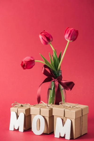 Bouquet of red tulips in glass vase and paper word mom on red background — Stock Photo