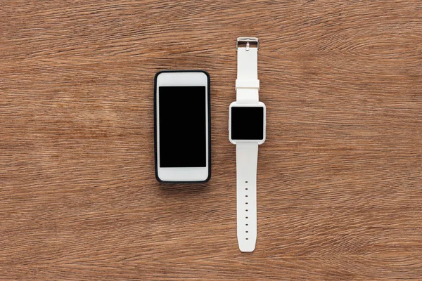 Top view of smartphone and smartwatch with blank screen on wooden background — Stock Photo