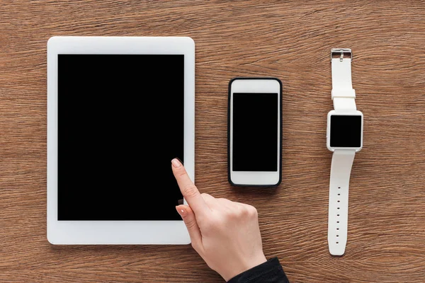 Vista recortada de la mujer con tableta digital, smartphone y smartwatch con pantalla en blanco sobre fondo de madera - foto de stock