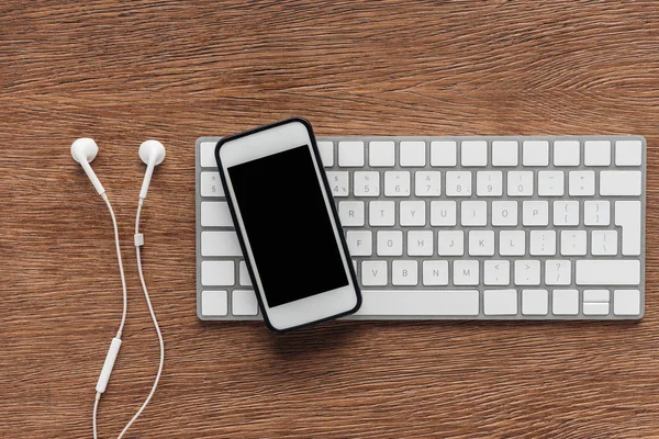 Vista superior del teclado, smartphone con pantalla en blanco y auriculares sobre fondo de madera - foto de stock