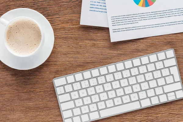 Vista superior de la taza de café, teclado y documentos sobre fondo de madera - foto de stock