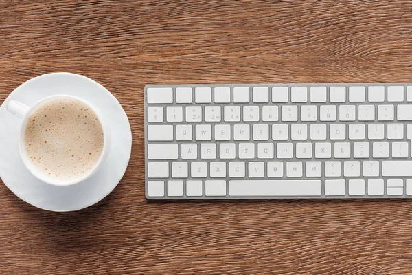 Vista superior da xícara de café e teclado portátil no fundo de madeira — Fotografia de Stock