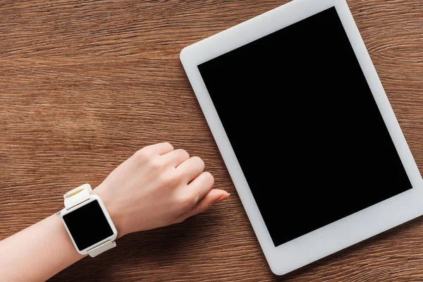 Partial view of girl with smartwatch and digital tablet with blank screen on wooden background — Stock Photo