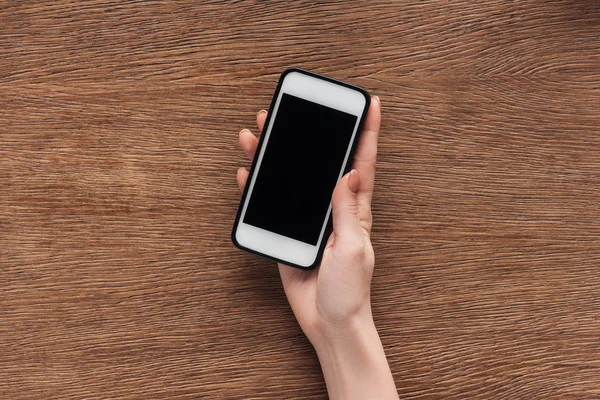 Vista parcial da mulher segurando smartphone com tela em branco no fundo de madeira — Fotografia de Stock