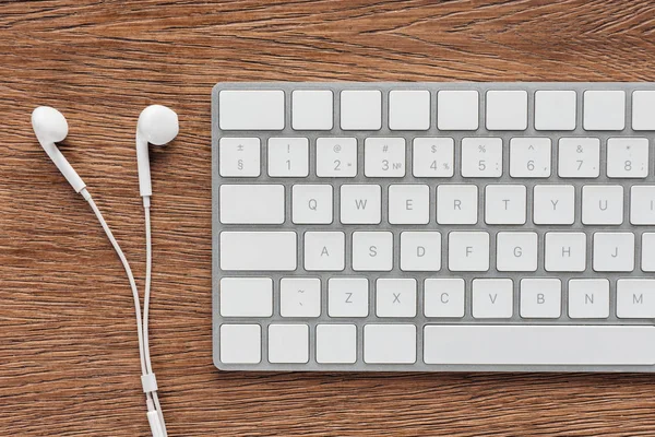 Top view of keyboard and earphones on wooden background — Stock Photo