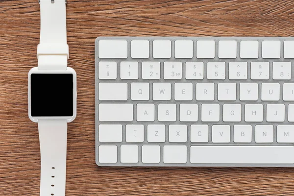 Visão superior do teclado e smartwatch com tela em branco no fundo de madeira — Fotografia de Stock