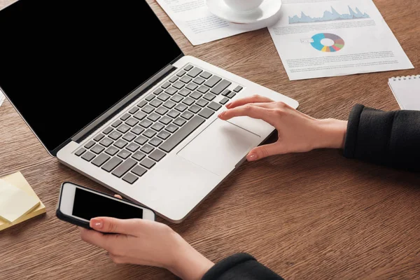 Vista recortada de la mujer usando teléfono inteligente y portátil con pantalla en blanco - foto de stock