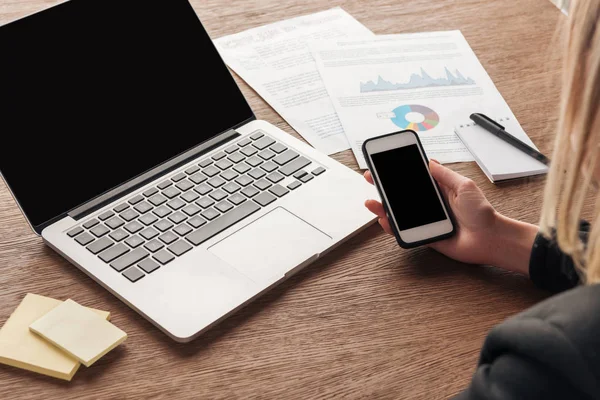 Vista parcial de la mujer usando smartphone con pantalla en blanco en el lugar de trabajo - foto de stock