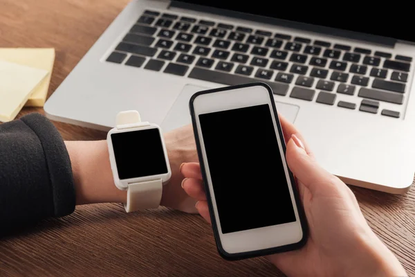 Partial view of woman with laptop, smartwarch and smartphone with blank screen — Stock Photo