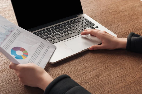 Ausgeschnittene Ansicht einer Frau, die Dokumente hält, während sie Laptop mit leerem Bildschirm benutzt — Stockfoto