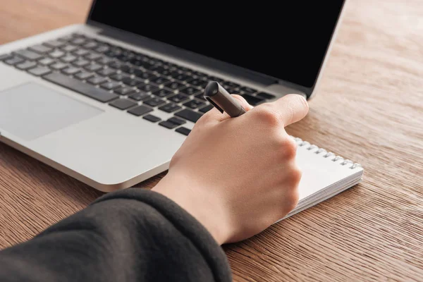 Cropped view of woman writing in notebook at workplace — Stock Photo