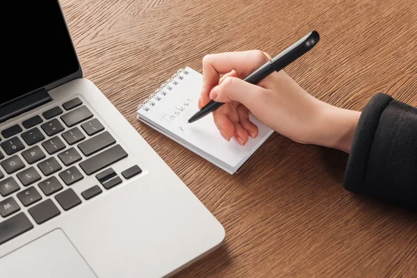 Vue recadrée de la femme écrivant dans un cahier à côté d'un ordinateur portable — Photo de stock