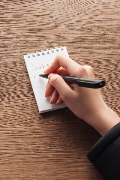 Cropped view of woman writing in notebook on wooden surface — Stock Photo
