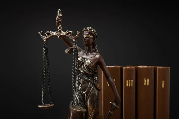 Bronze statuette with scales of justice and volumes of brown books isolated on black — Stock Photo