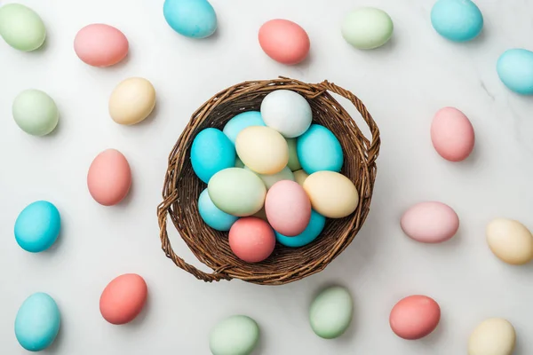 Vue de dessus des œufs de Pâques pastel éparpillés et panier en osier sur blanc — Photo de stock