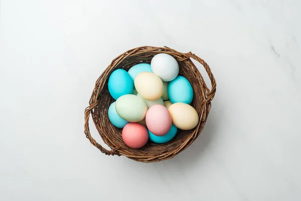 Blick von oben auf bunte pastellfarbene Ostereier im Weidenkorb auf Weiß — Stockfoto