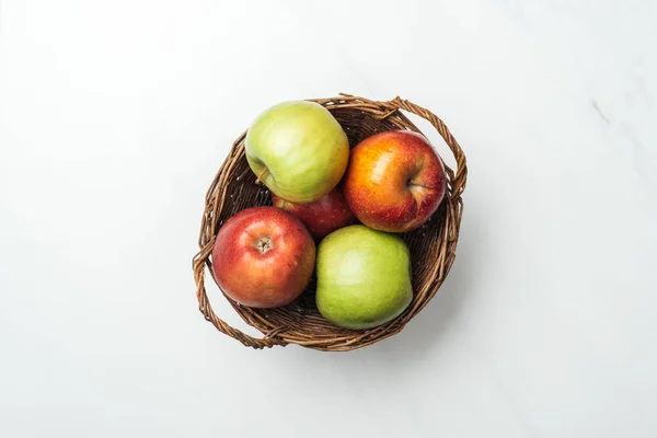 Vista superior de manzanas rojas y verdes en canasta de mimbre sobre blanco - foto de stock