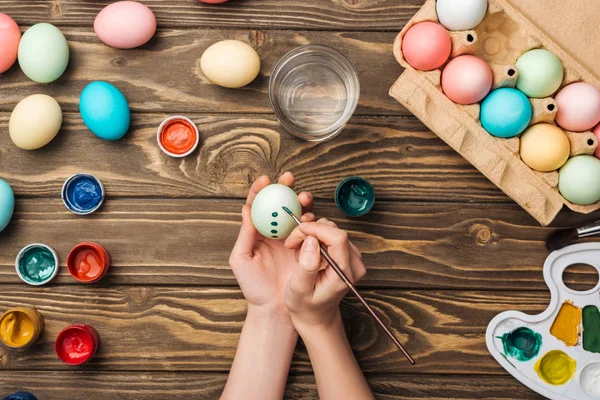 Частичный вид девушки, украшающей пасхальные яйца за деревянным столом красками и цветовой палитрой — стоковое фото