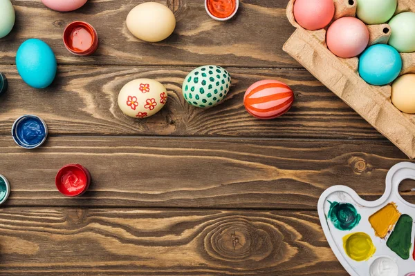 Top view of painted easter eggs, color palette and acrylic paints on wooden surface with copy space — Stock Photo