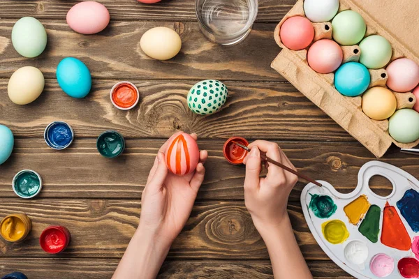 Vista parziale della donna che dipinge uova di Pasqua al tavolo di legno con vernici e tavolozza dei colori — Foto stock