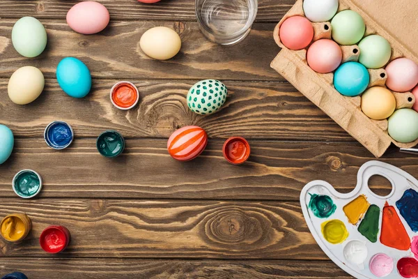 Top view of painted easter eggs, color palette and acrylic paints on wooden surface — Stock Photo