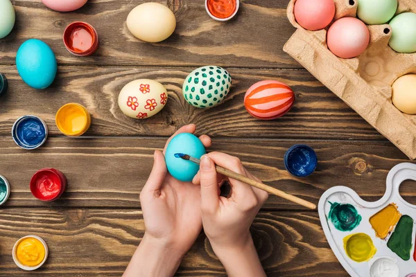 Vista recortada de la mujer pintando huevos de Pascua en la mesa de madera con pinturas y paleta de colores - foto de stock