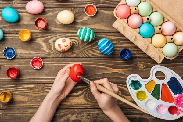 Top view of girl painting easter eggs at wooden table with paints and color palette — Stock Photo