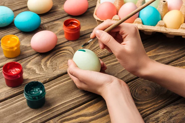 Teilansicht einer Frau, die Ostereier am Holztisch mit Pinsel verziert — Stockfoto