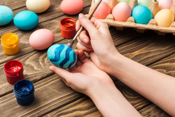 Vista recortada de la mujer decorando huevos de Pascua con pincel en la mesa de madera - foto de stock