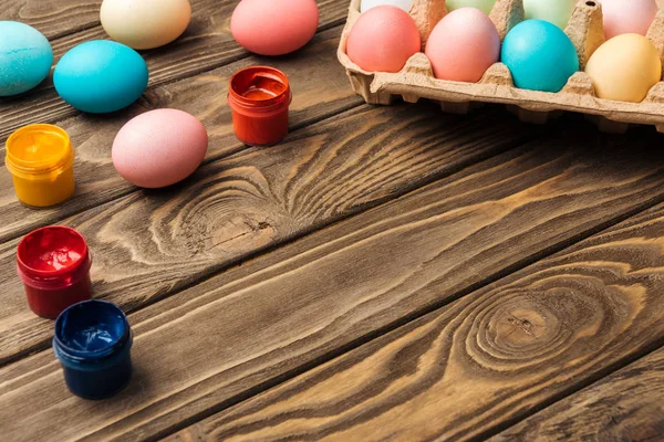 Pastel easter eggs in cardboard box with acrylic paints on wooden table with copy space — Stock Photo