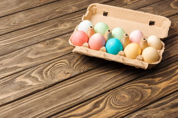 Ovos de Páscoa pastel em caixa de papelão na superfície de madeira com espaço de cópia — Fotografia de Stock
