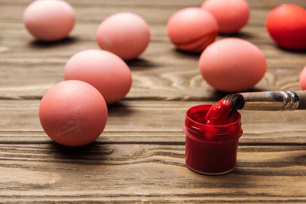Foyer sélectif des œufs de Pâques roses avec peinture et pinceau sur table en bois — Photo de stock