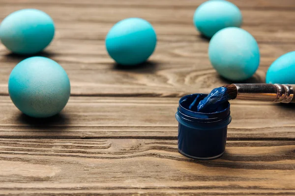 Selective focus of pastel blue easter eggs, paints and paintbrush on wooden surface — Stock Photo