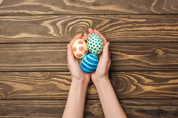 Top view of woman holding easter eggs with pattern on wooden surface — Stock Photo