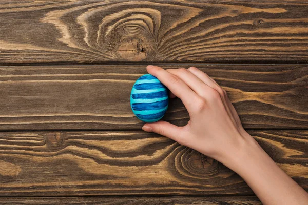Vista superior da mulher segurando ovo de Páscoa com padrão na superfície de madeira — Fotografia de Stock