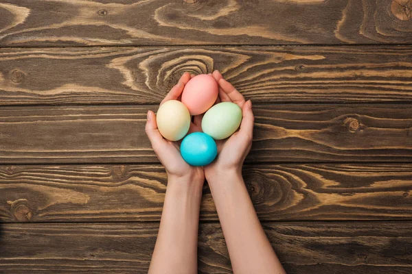 Vista superior de la mujer sosteniendo huevos de Pascua pastel en la superficie de madera - foto de stock