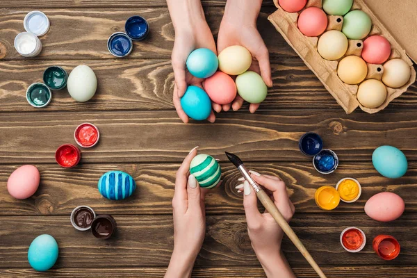 Vista dall'alto delle donne che tengono e dipingono uova di Pasqua a tavola di legno — Foto stock