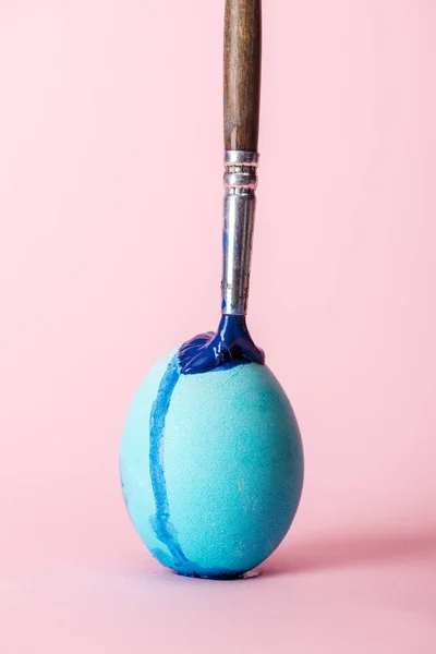 Huevo de Pascua con pintura azul y pincel en rosa - foto de stock