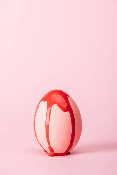 Easter egg with red paint spills on pink with copy space — Stock Photo