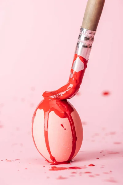 Foyer sélectif de l'oeuf de Pâques avec des déversements de peinture rouge et pinceau sur rose — Photo de stock