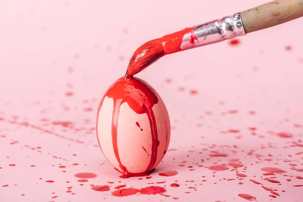 Osterei mit roten Farbklecksen und Pinsel auf rosa — Stockfoto