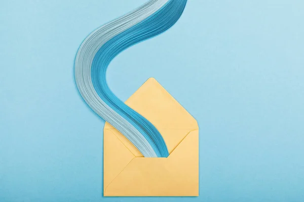 Top view of blue curved abstract paper lines and yellow envelope on blue background — Stock Photo