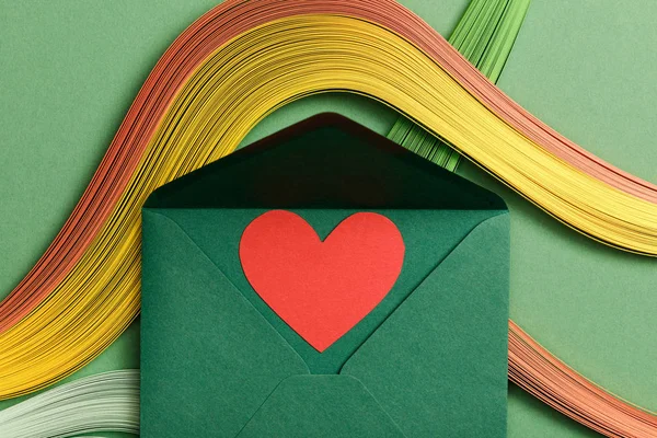 Vista superior de linhas abstratas multicoloridas em fundo verde com envelope aberto verde e sinal de coração — Fotografia de Stock